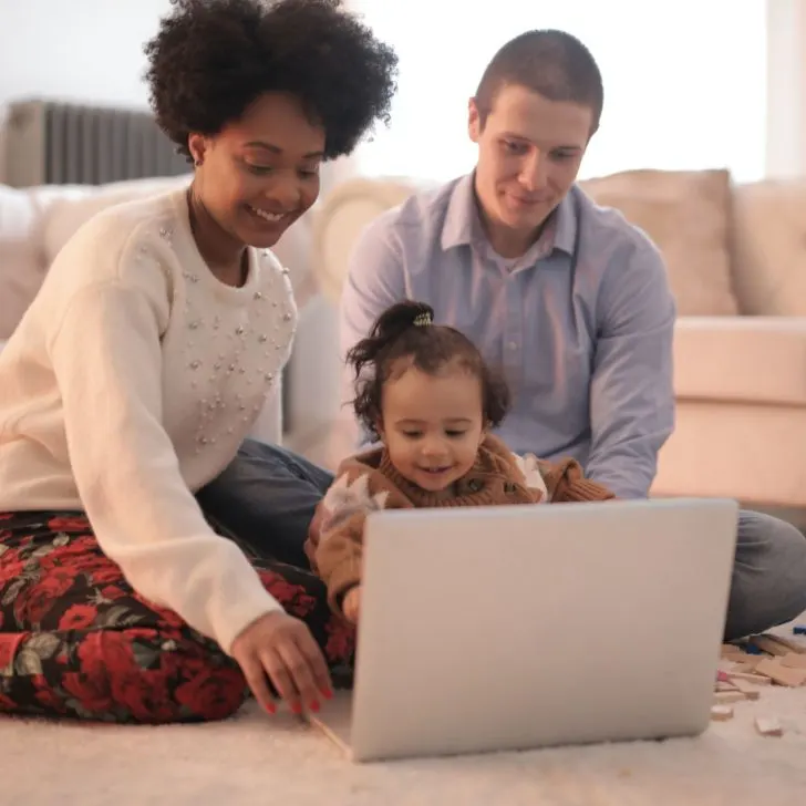 A toddler sits comfortably in a lap with a laptop, happily interacting with the computer.