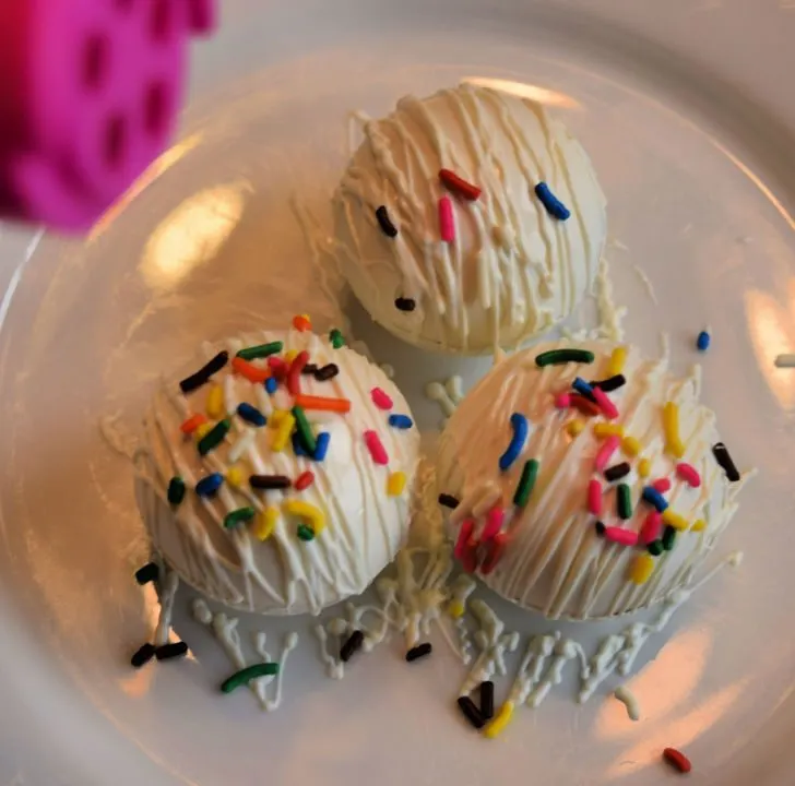 A plate of colorful cupcakes topped with buttercream icing, sprinkles, nonpareils, and food coloring indoors, ready for cake decorating.
