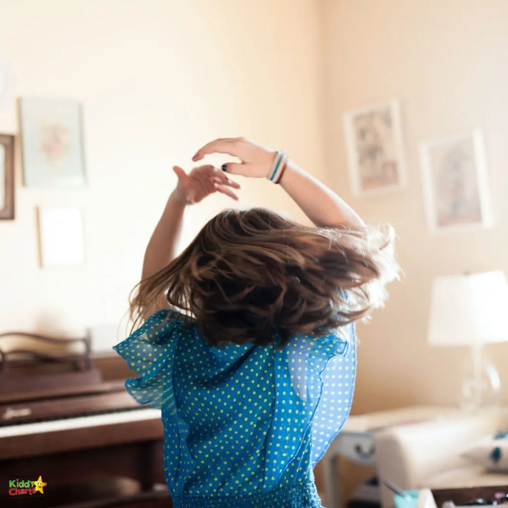 A child in a blue polka-dotted dress is joyfully twirling, with hair flying, in a warmly lit room featuring elegant furniture and framed artwork.