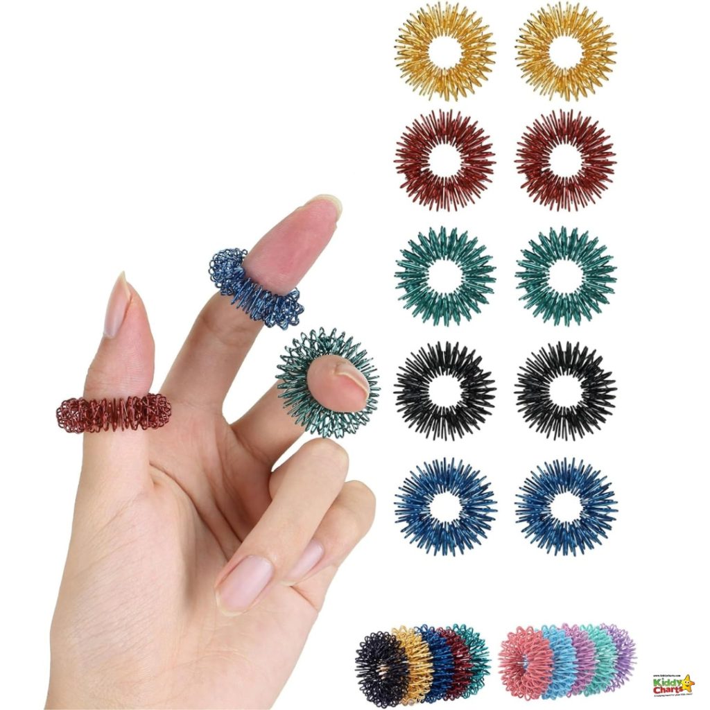 A person's hand displays two ring-style woven finger massagers. Multiple colorful massagers are arrayed around in various colors and patterns.