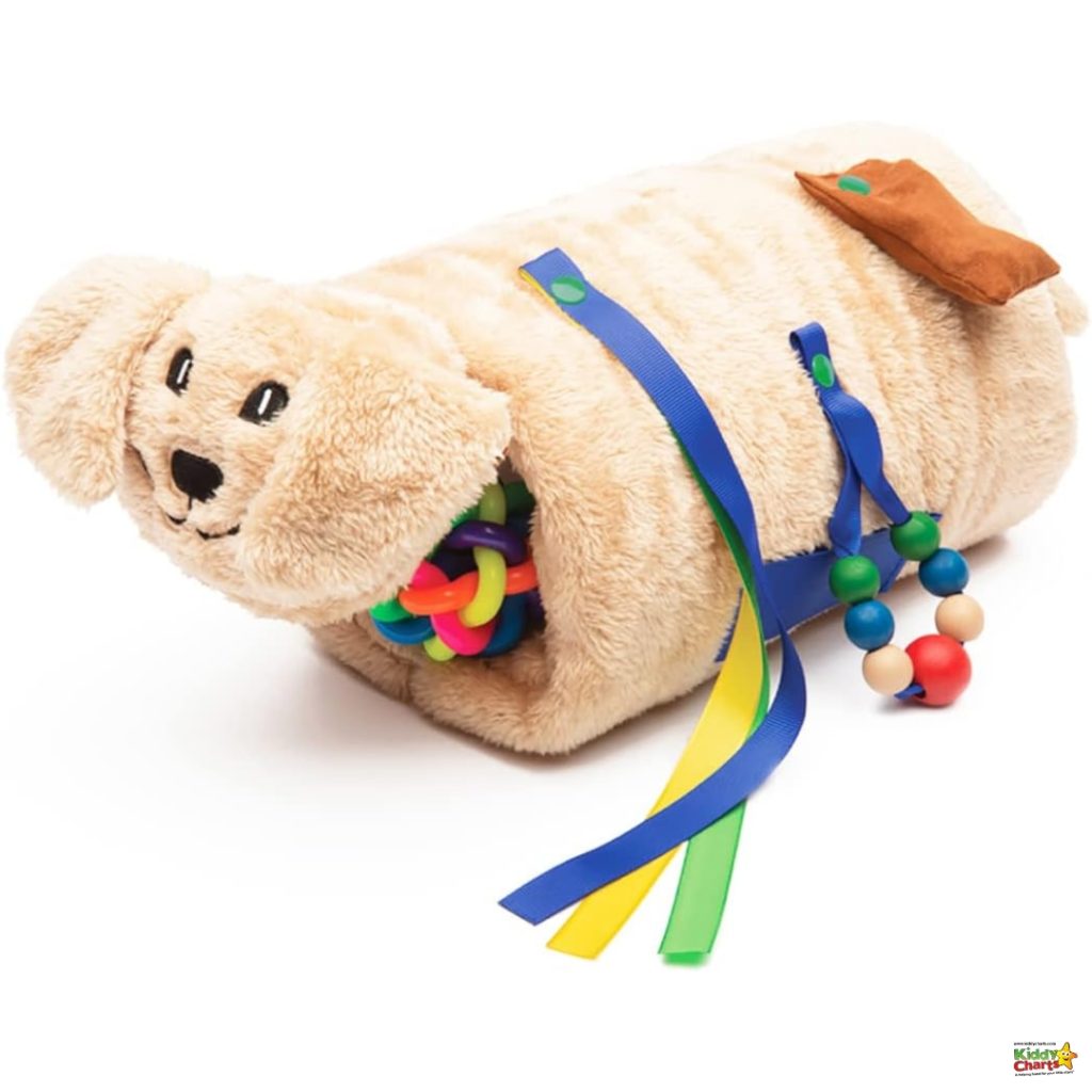 A plush toy dog designed as a sensory activity toy, with various colorful ribbons, rings, and beads attached for tactile and visual stimulation.