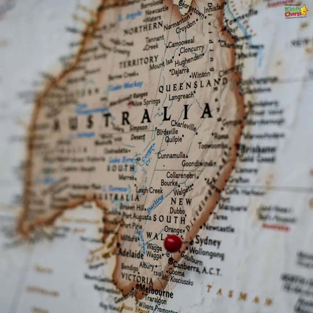 This image features a close-up of a weathered map of Australia with a red pin marking a location, towns and routes visible, and depth of field blurring the edges.