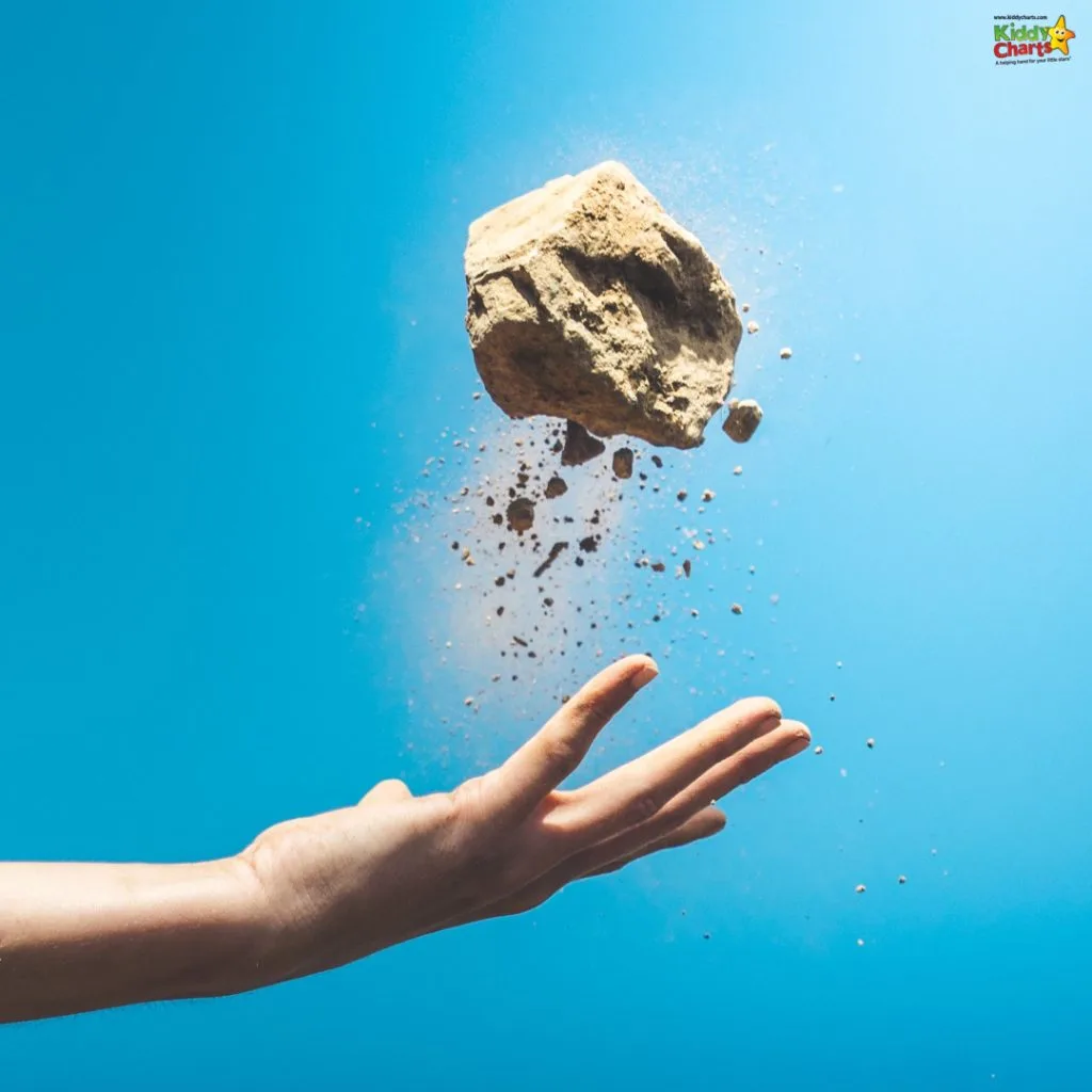 A person's hand is tossing a large rock into the air against a clear blue sky, capturing the dirt debris scattering from its surface.