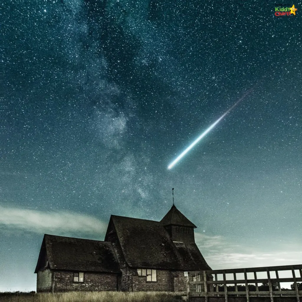 A shooting star blazes across a starry night sky over an old, dark church building, possibly in a rural setting, under the Milky Way.