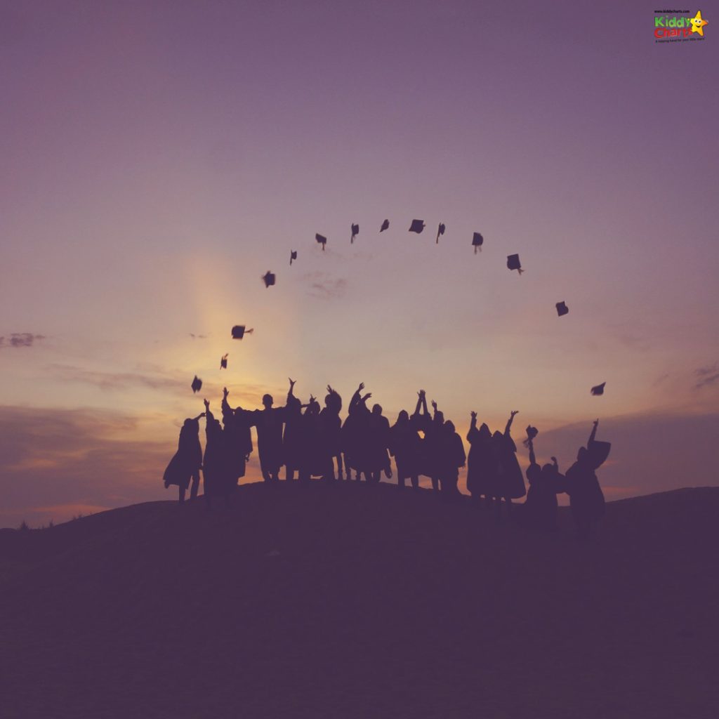 A group of people celebrates on a hill, silhouetted against a sunset sky, joyously throwing their graduation caps into the air.