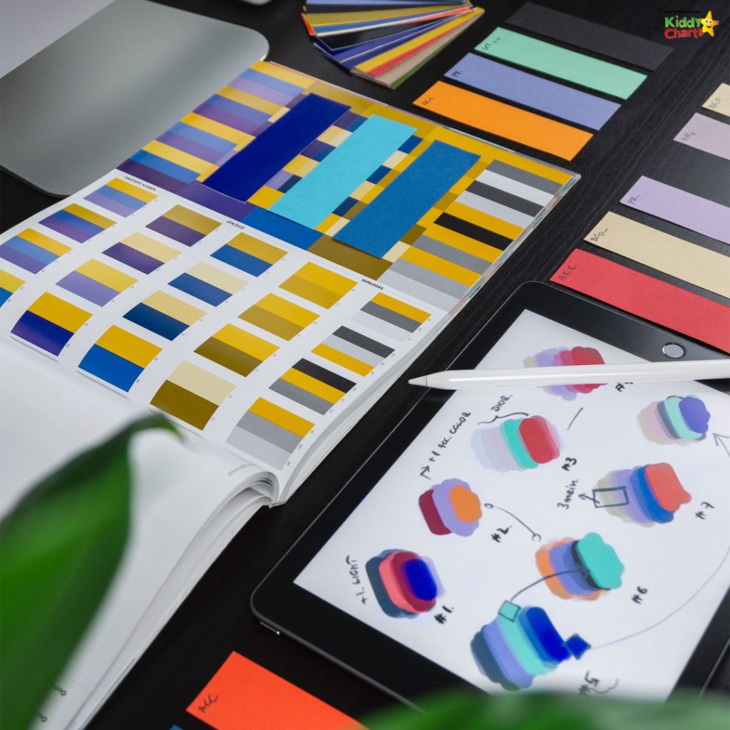 An organized desk with color palettes, design charts, a digital tablet displaying graphics, and color samples for creative design work.