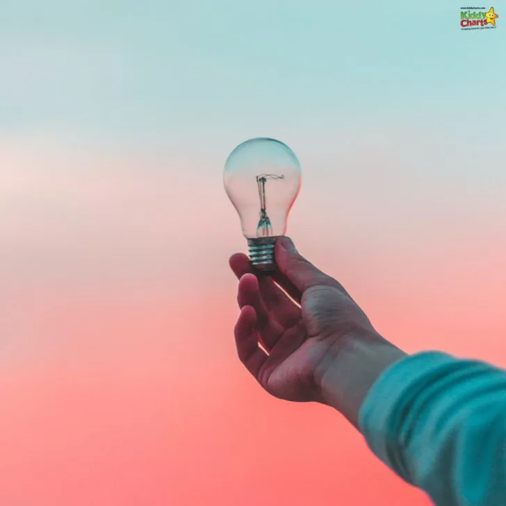 A person's hand holds a clear lightbulb against a soft pastel sky with pink and blue hues, giving the illusion the bulb is lit by the sky.