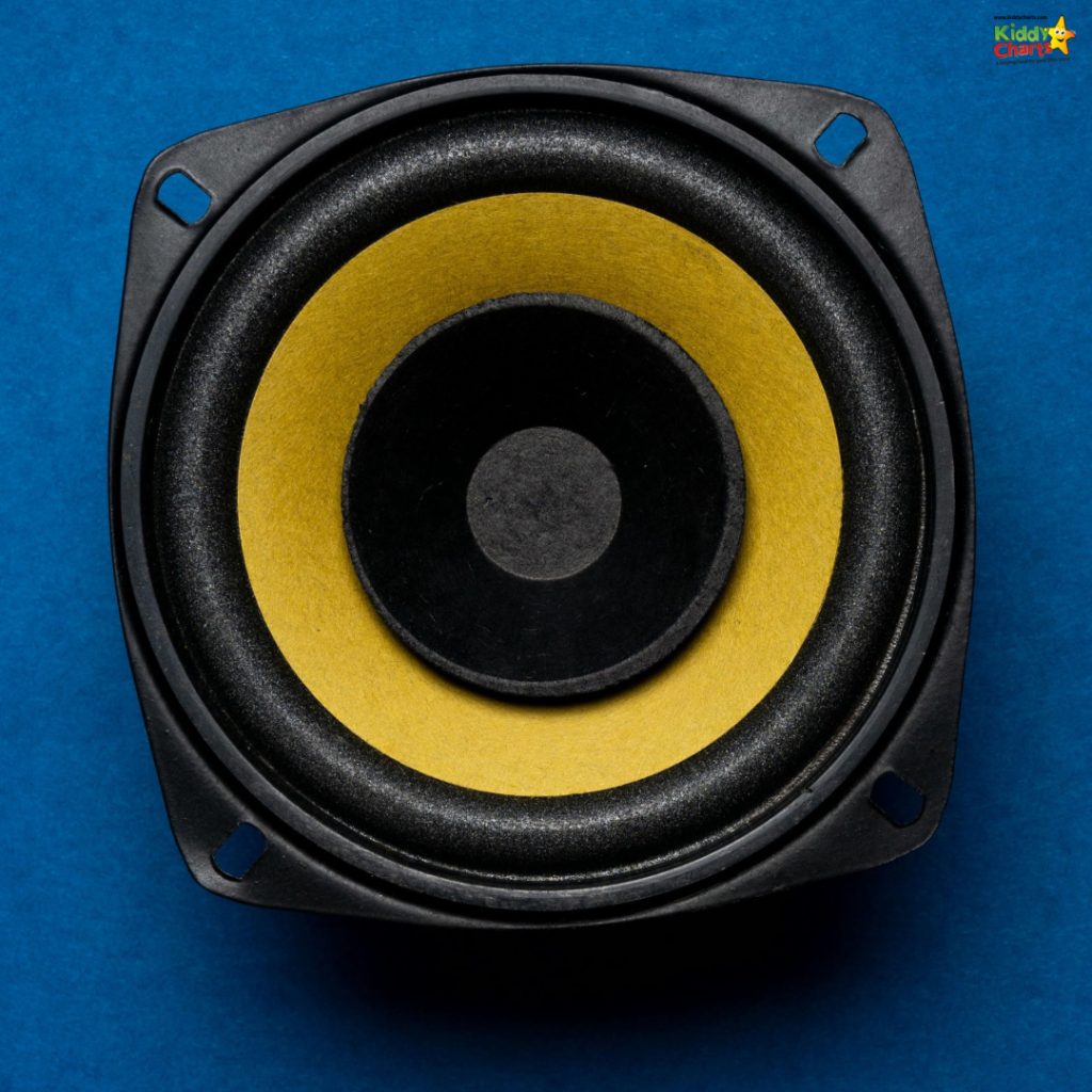 This is a close-up image of a black square loudspeaker with a yellow cone, placed on a bright blue background, viewed directly from above.