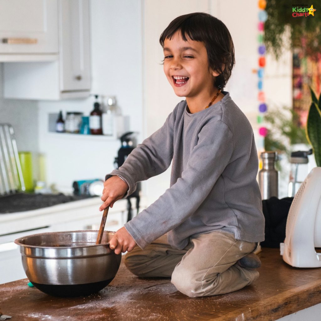 A cheerful child sits on a kitchen counter, mixing ingredients in a bowl, surrounded by baking equipment. The environment appears homey and filled with natural light.