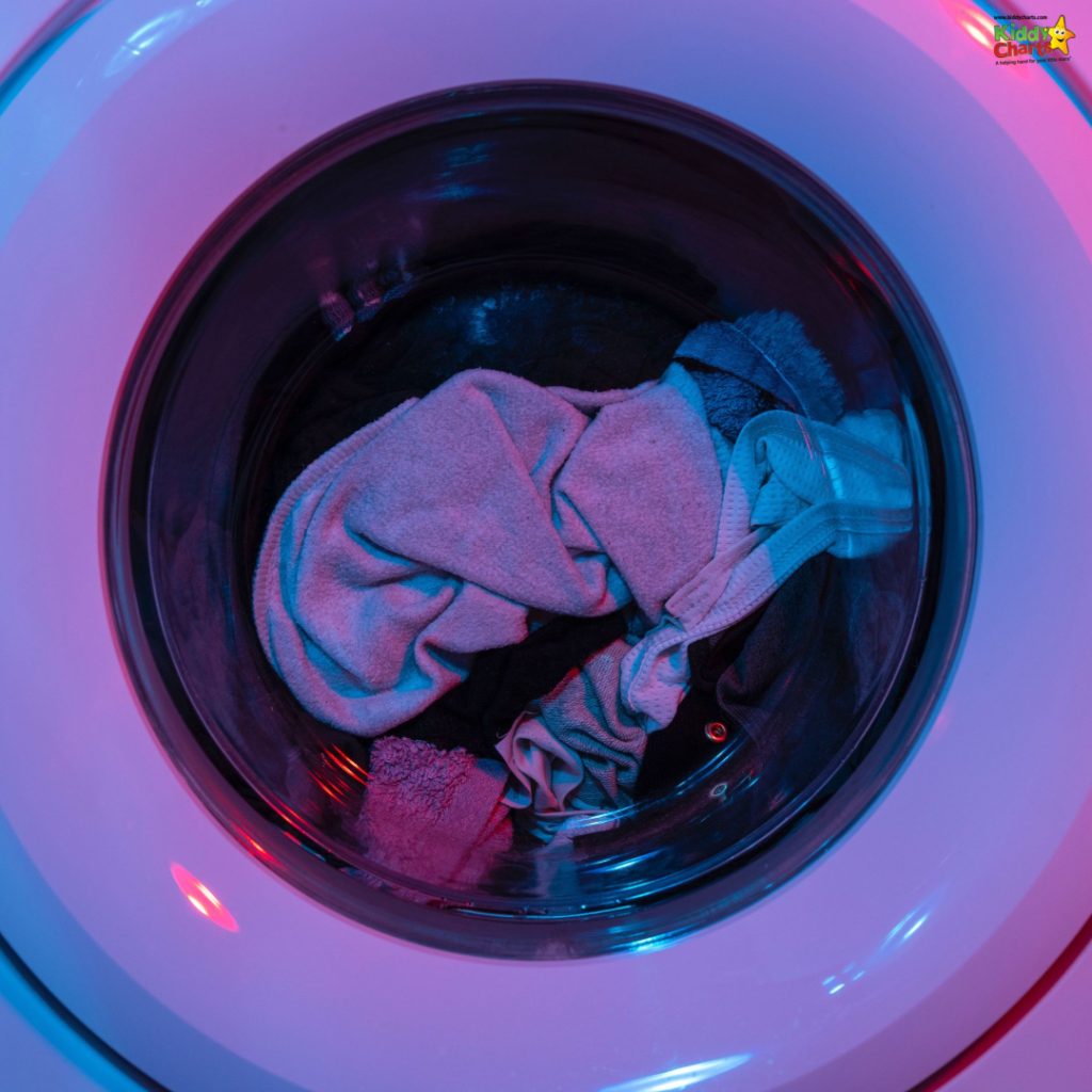 A front-loading washing machine with clothes inside illuminated by blue and pink lighting, creating a neon-like glow. The image conveys a modern, clean vibe.