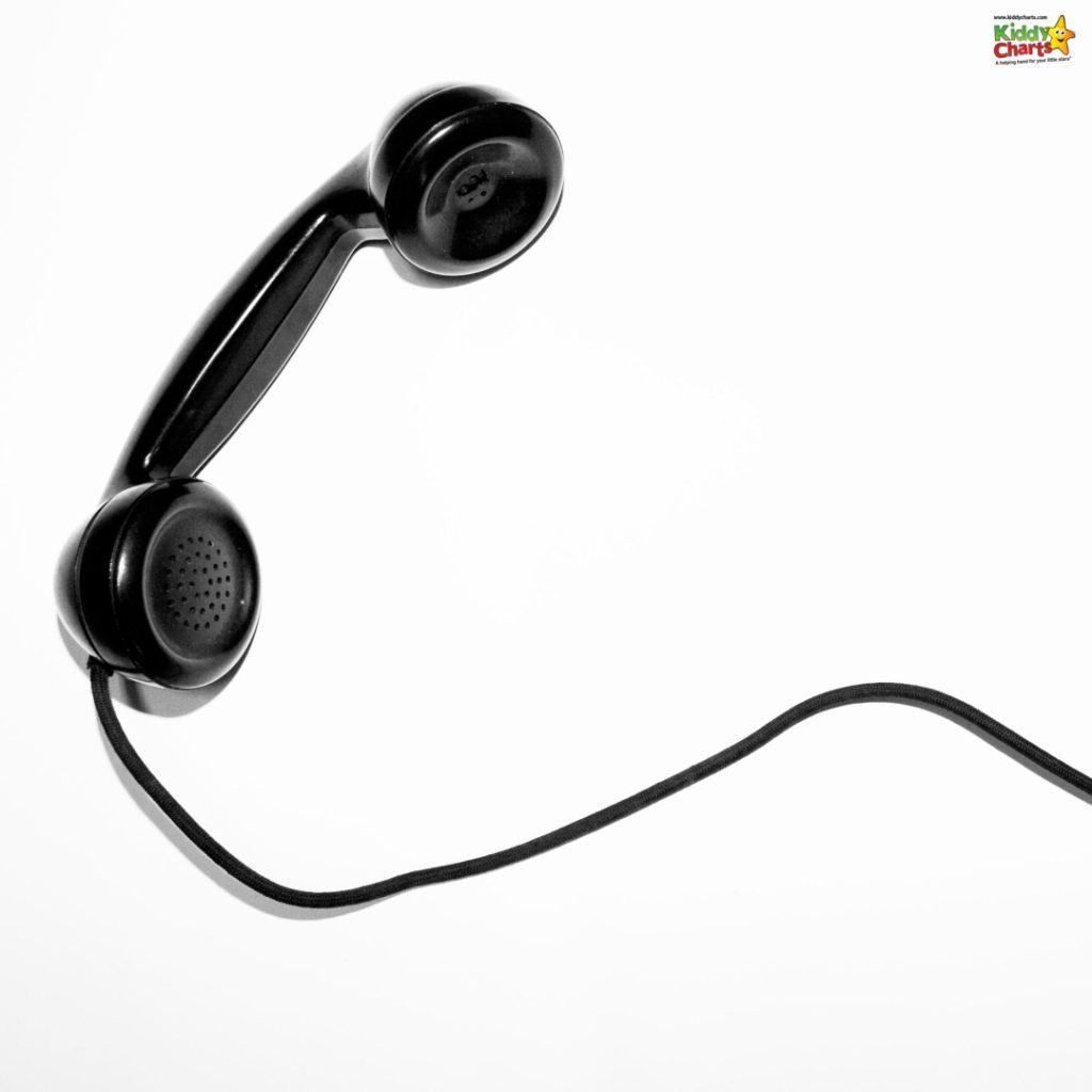 An old-fashioned black telephone handset suspended in mid-air against a white background, with its cord casually drooping below it.