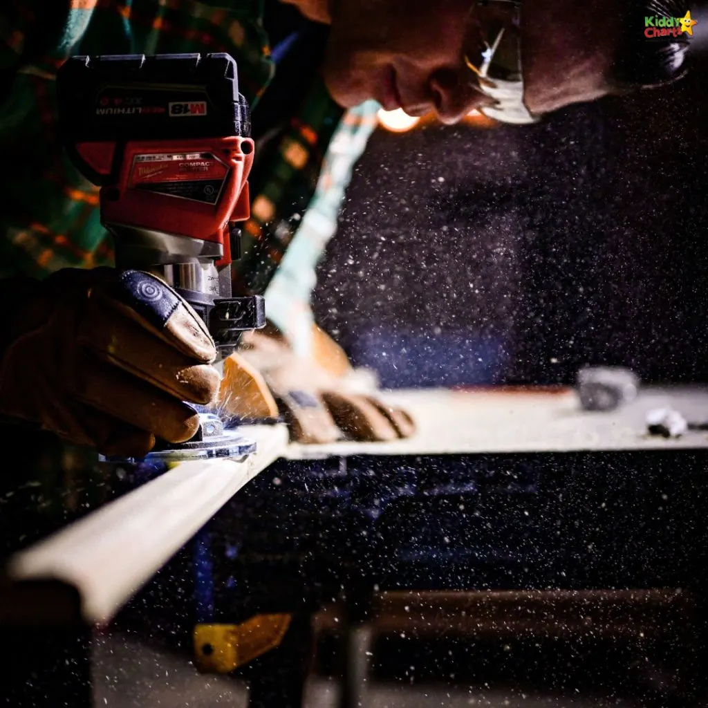 A person wearing safety glasses and gloves uses a red power drill on wood, creating a cloud of sawdust illuminated by bright light.