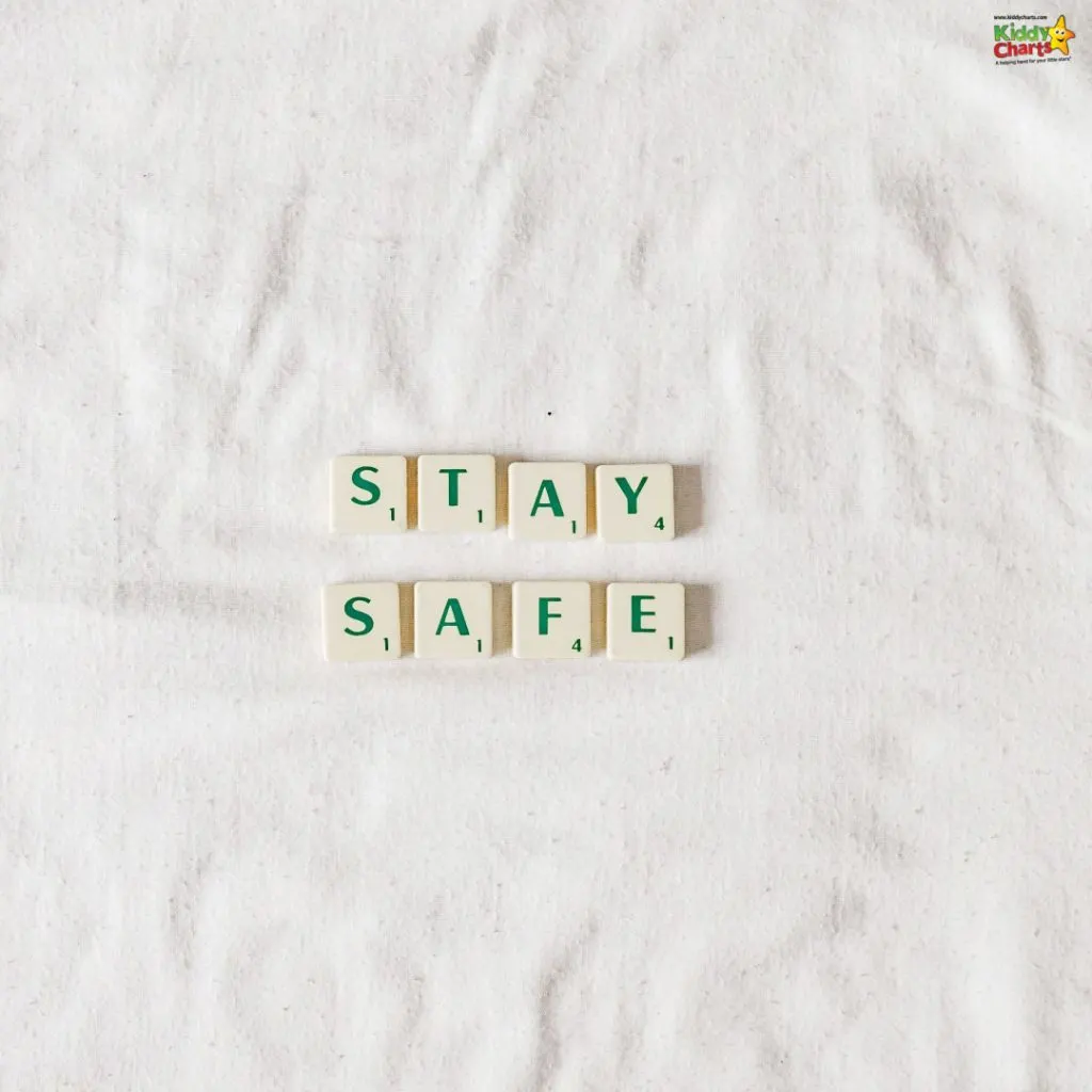 The image shows Scrabble tiles arranged on a textured white background spelling out the words "STAY SAFE."